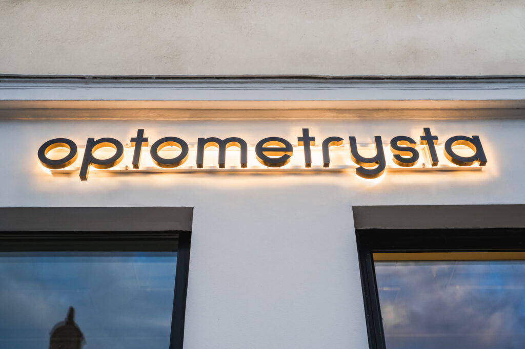 Napis „optometrysta" w technice halo na jasnej elewacji